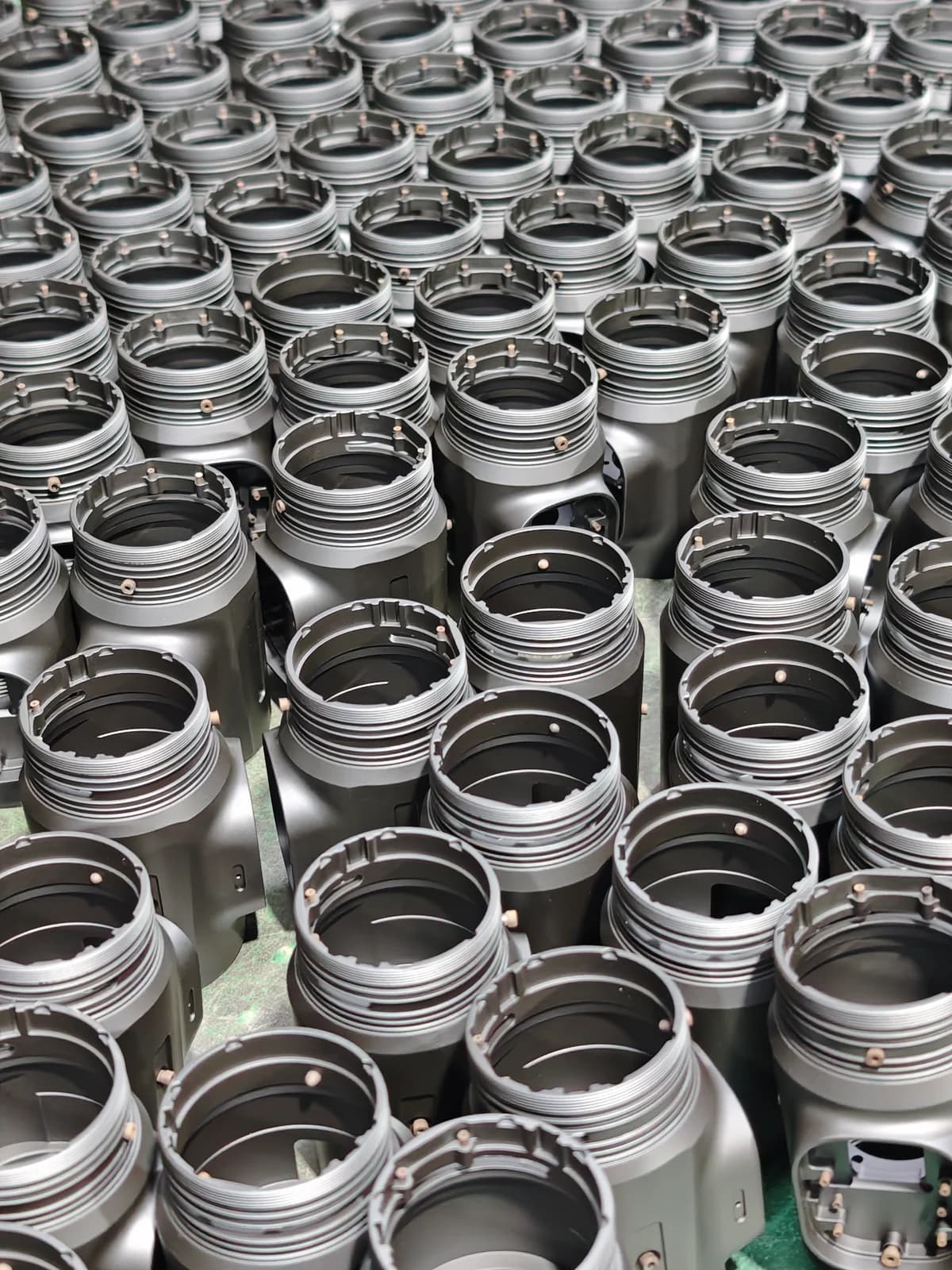 Batch of dark metal housings arranged together on a work surface.